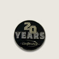 A round black and silver 20th anniversary lapel pin for Centershot, featuring a black enamel background with silver and gold-toned lettering.