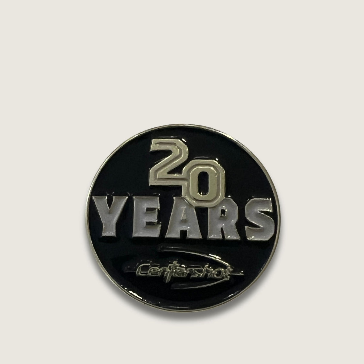 A round black and silver 20th anniversary lapel pin for Centershot, featuring a black enamel background with silver and gold-toned lettering.