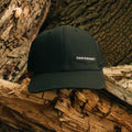 A black trucker hat with a black mesh back and a small black patch on the front that reads 'CENTERSHOT' in white, resting on weathered tree logs outdoors.