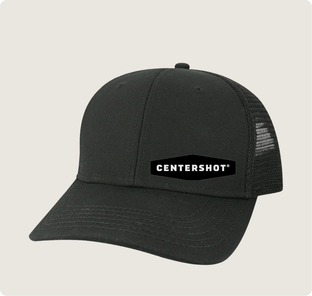 A black trucker-style baseball cap with a curved brim, black mesh back panels, and a black rectangular patch on the front that reads 'CENTERSHOT' in white text, shown on a light gray background.
